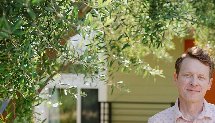 Man in pink shirt standing with hands in pockets in front of home.