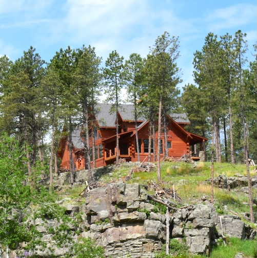 Large, red, wood cabin in South Dakota on a small cliff, perhaps a vacation home.