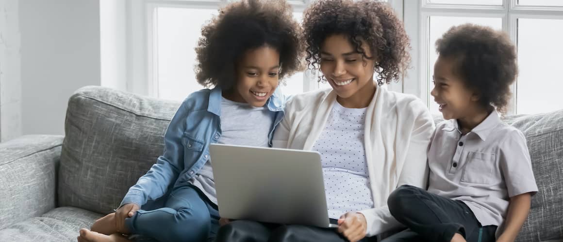 A Black woman with her daughters on a couch, looking at a computer, potentially in a home setting.