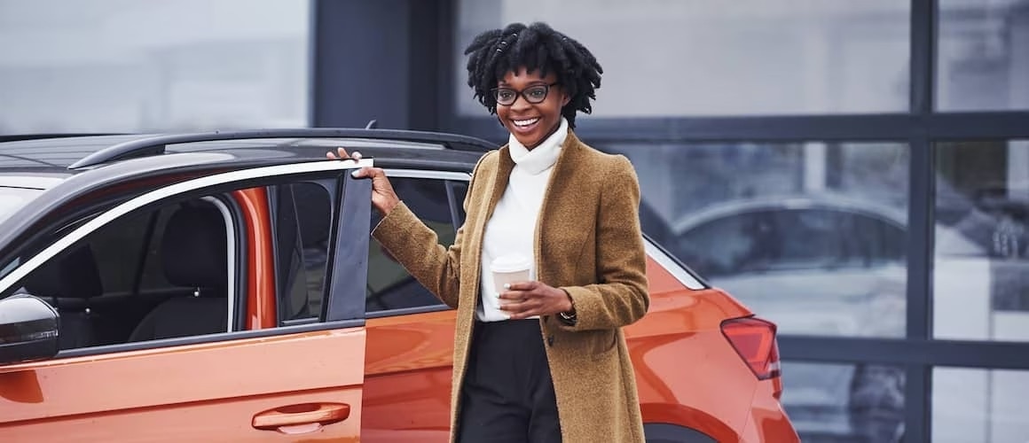 African american woman in brown coat opens doors to get into a orange car