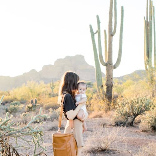 Woman with baby in southwestern landscape featuring large cacti and mountains in background.