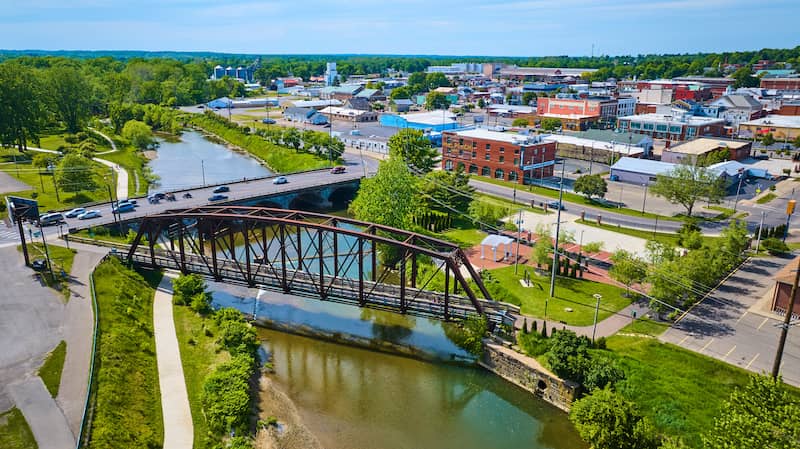 Aerial view of Mount Vernon, Ohio showcasing a town with streets, buildings, and green spaces surrounded by hills and trees.