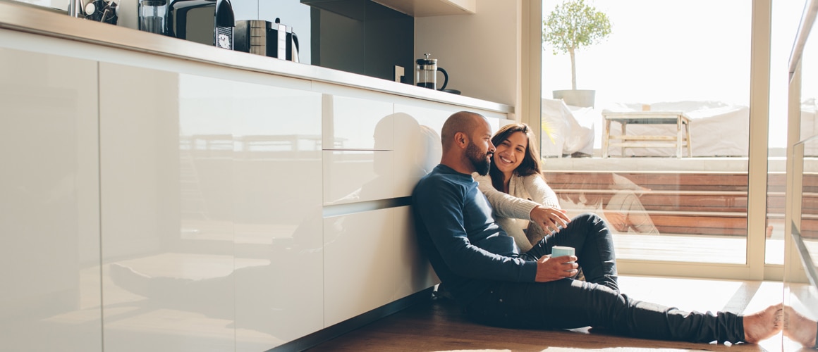 A man and women sitting on the floor of kitchen smiling.