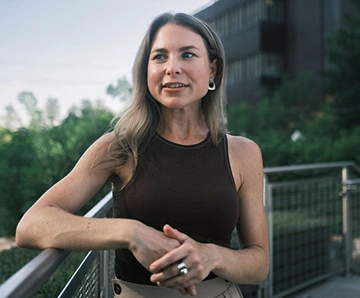 A white woman talking outside while standing on a bridge surrounded by buildings. Analytics click: “rocket mortgage: full funnel purchase campaign: popular next steps: purchase rates page.