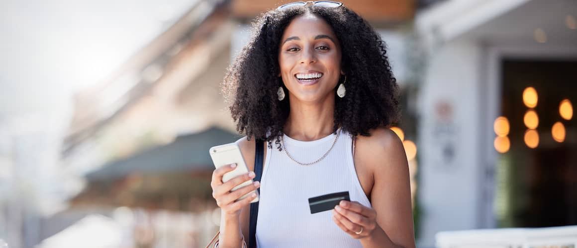 Woman holding credit card smiling while out shopping.