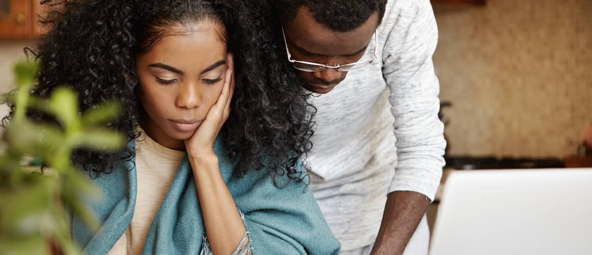 Couple looking over their finances together with pensive looks on their faces.