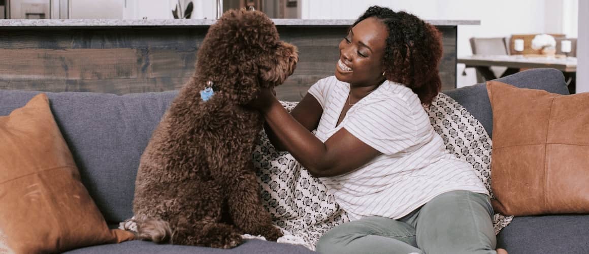 Woman smiling while petting her brown labradoodle on her couch.