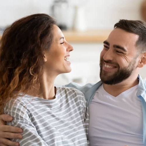 A couple smiling and talking while sitting on the couch in their house.