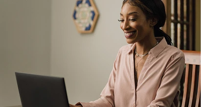 Black woman smiles while researching refinance options on her laptop.