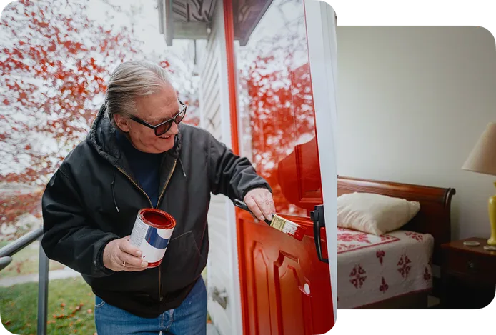 Older adult painting a red front door outside a home