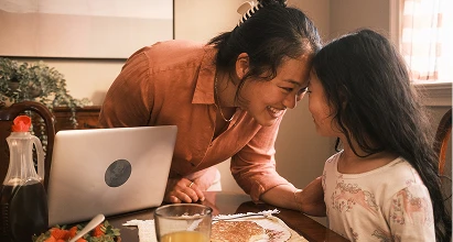 Mother and daughter smiling while touching foreheads at the breakfast table.