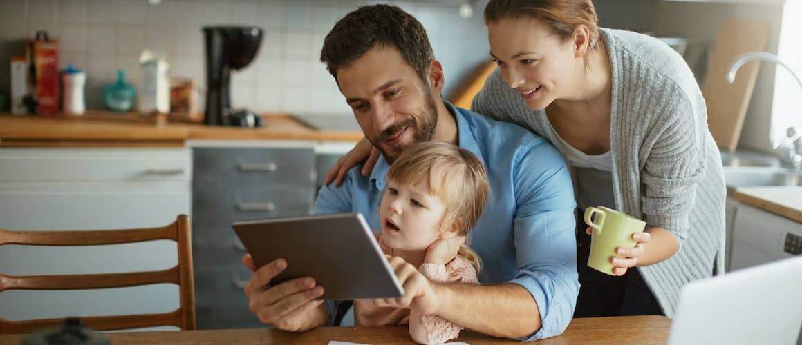 Young family looking at tablet at kitchen table.