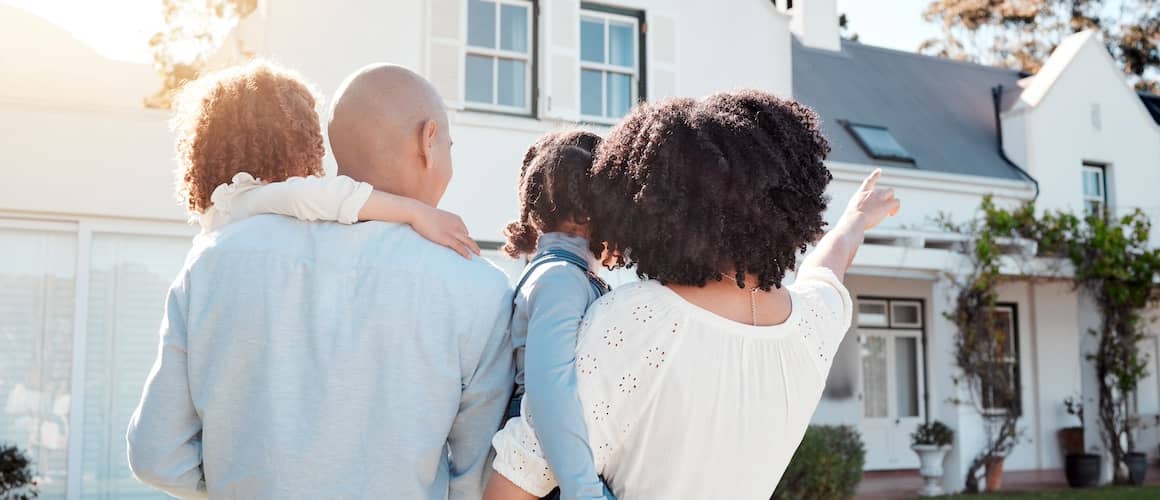 Family of four standing outside their new home with their backs to the camera.