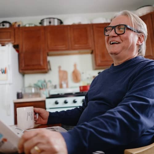 Man in kitchen with newspaper laughing.