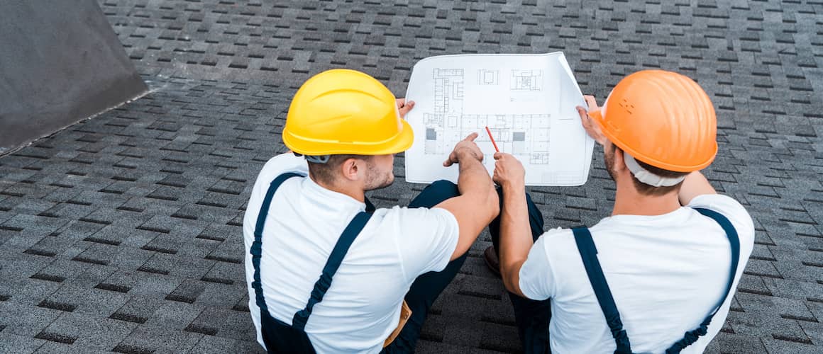 Roofers sitting on roof reviewing blueprints.