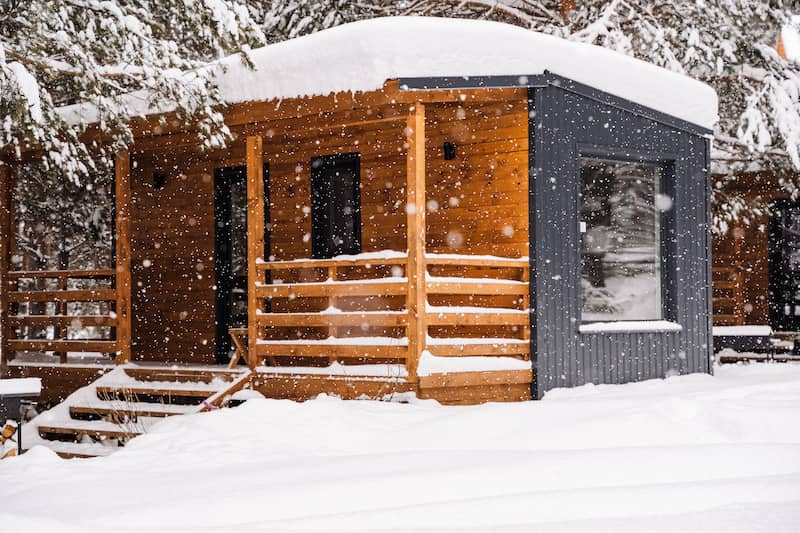 Modular home with large windows and cabin-esque porch in winter.