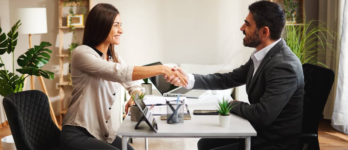 A stock photo portraying a woman shaking hands with a man, potentially in a real estate or home buying context, possibly indicating agreement or partnership.