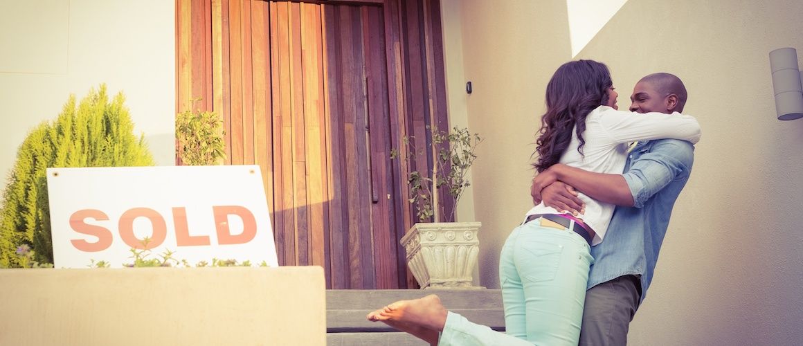 A young couple standing in front of their new home, symbolizing homeownership and a new chapter in life.