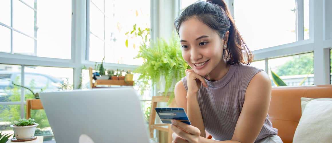 Young woman with peaceful look on her face, holding a credit card and working on her open laptop in her home.