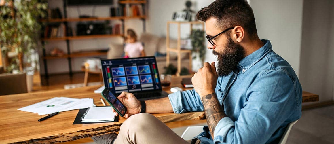 Man sitting at desk at home in front of laptop while checking his phone.