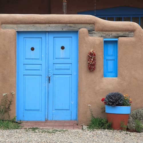 Taos New Mexico historic traditional adobe home with bright blue doors and hanging ristra.