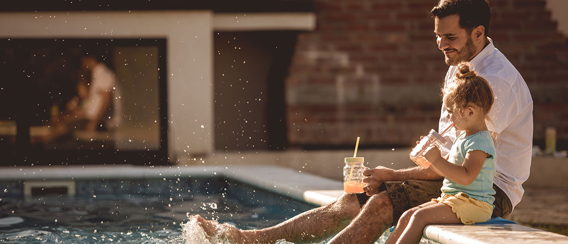 A father and daughter sitting by a pool, enjoying a relaxing moment together in a sunny setting.