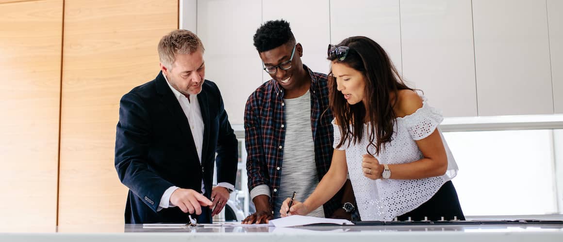 Interracial couple with a realtor, signing, possibly representing a diverse couple finalizing a real estate deal with a realtor.