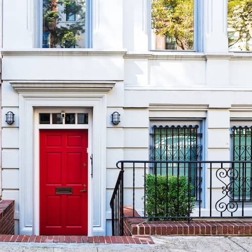 White limestone Manhattan townhome with red door and black wrought iron gate.