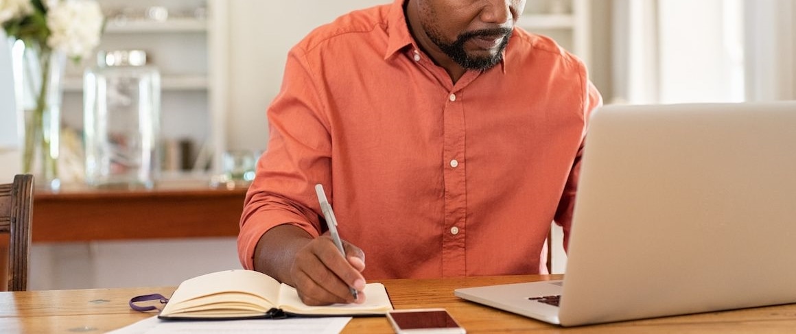 Man writing finances in a notebook, indicating budgeting or financial planning.