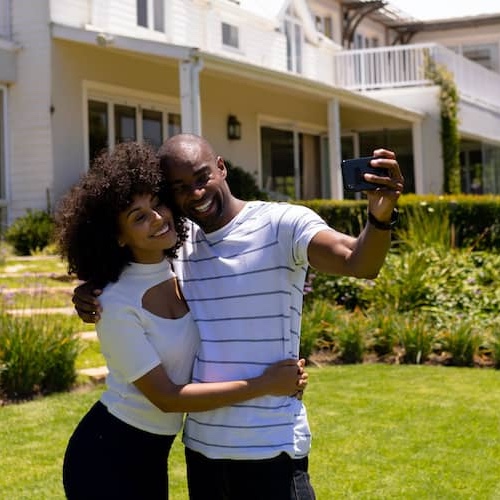 Couple posing and taking a picture outside their home.