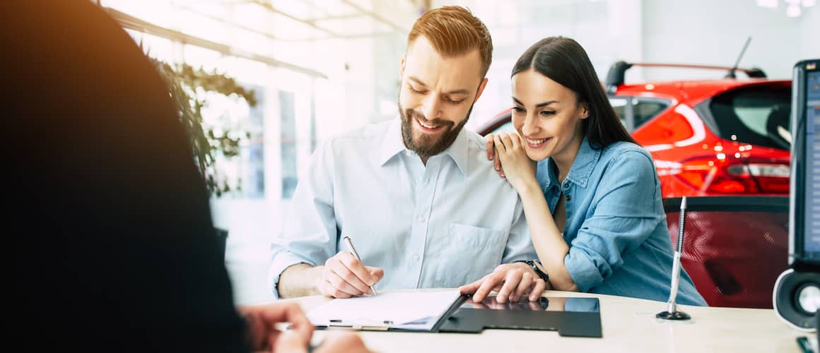 Young couple signing documents at car dealership.