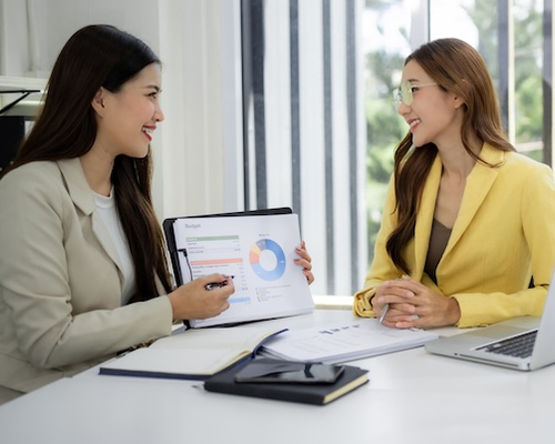 Two woman go over budget charts together, possibly discussing how to plan monthly mortgage payments.