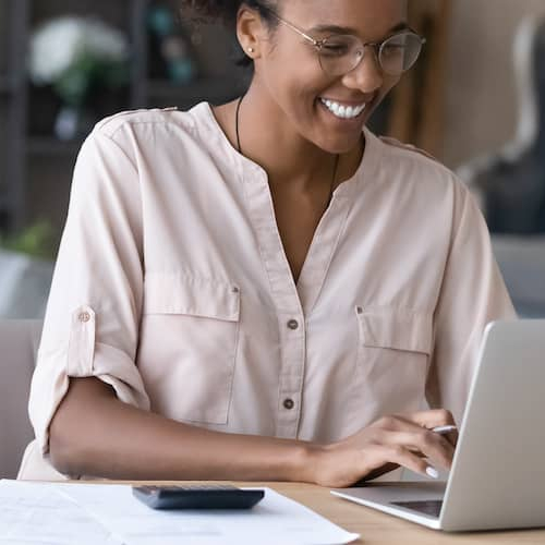 A happy millennial African American woman managing household budget and finances.
