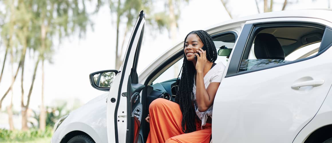 Young woman chatting on phone and getting out of her white new car.