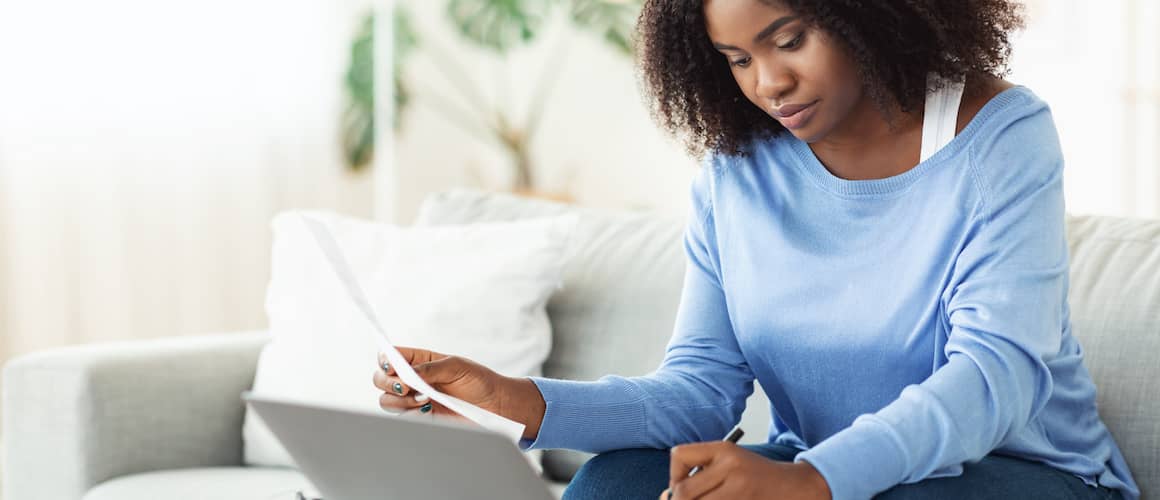 Woman sitting on couch going over her budget on laptop.