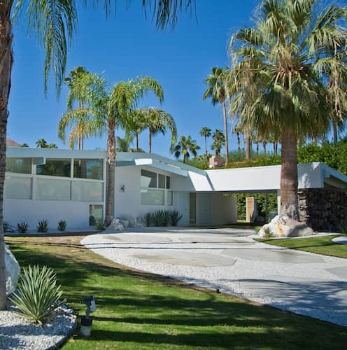 Palm Springs midcentury modern ranch style home in white with large front yard landscaped with palm trees.