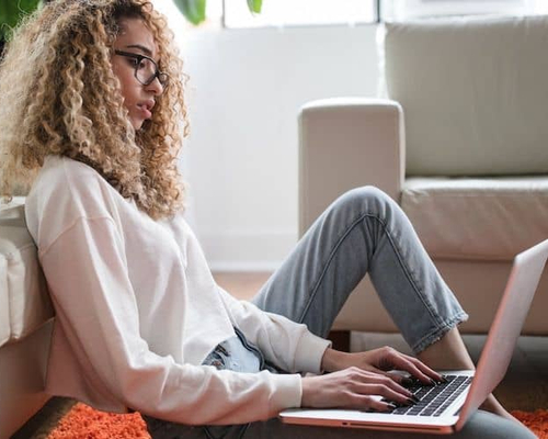 Woman sitting against couch, reviewing loan offers on computer.