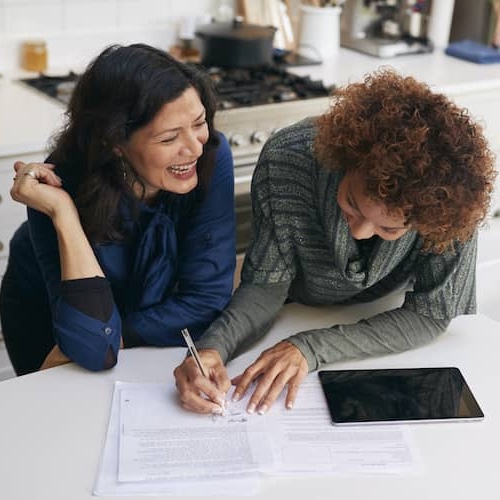 Two women in a kitchen writing on papers.