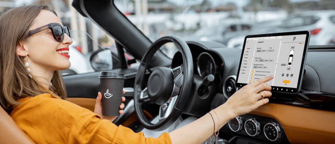 Cheerful woman controlling car with a digital dashboard and holding a coffee tumbler.