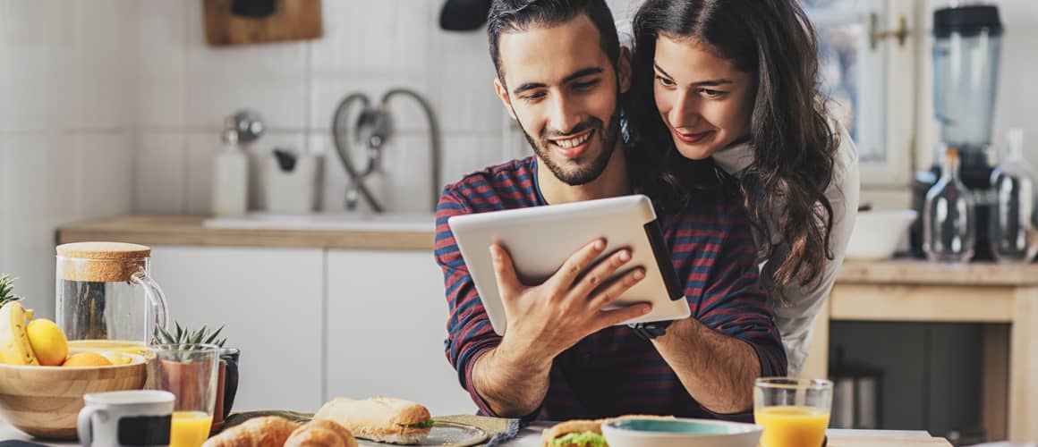 A couple looking at an iPad in a kitchen.