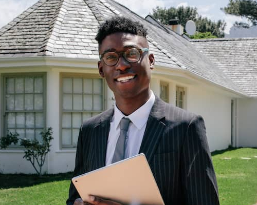 A real estate agent holding an iPad standing in front of a house possibly advertising it for sale.