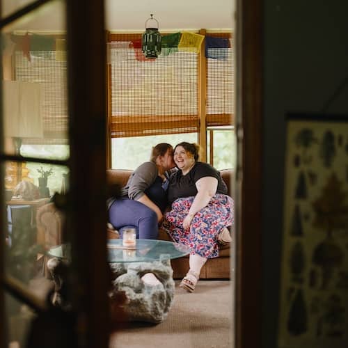 View through inside door of couple sitting on couch smiling.