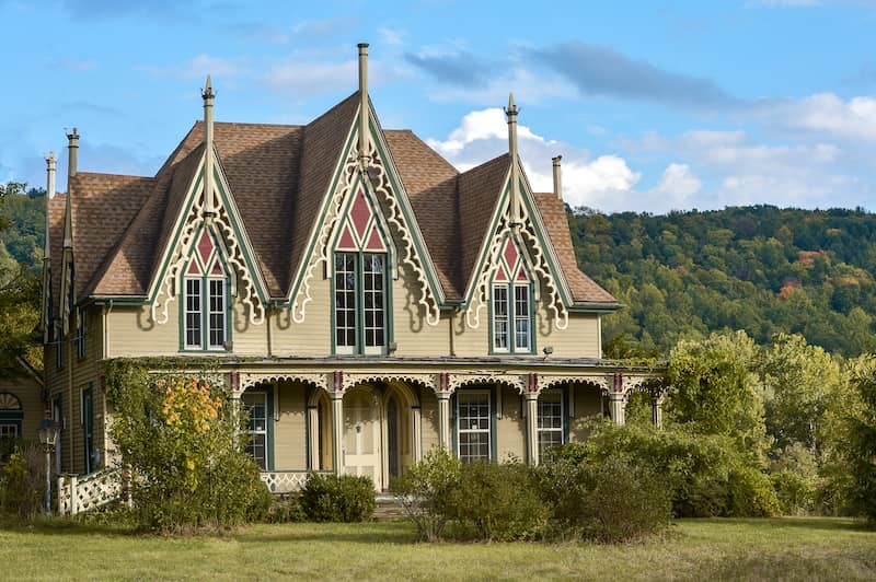 Exterior view of a tan gothic revival style home with large front porch.