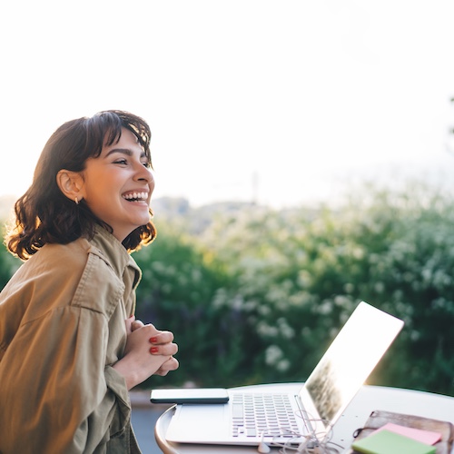 Young woman working remotely outside on laptop, smiling.