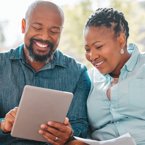 A mature couple looking through their bills while using a digital tablet, possibly managing finances or household expenses.