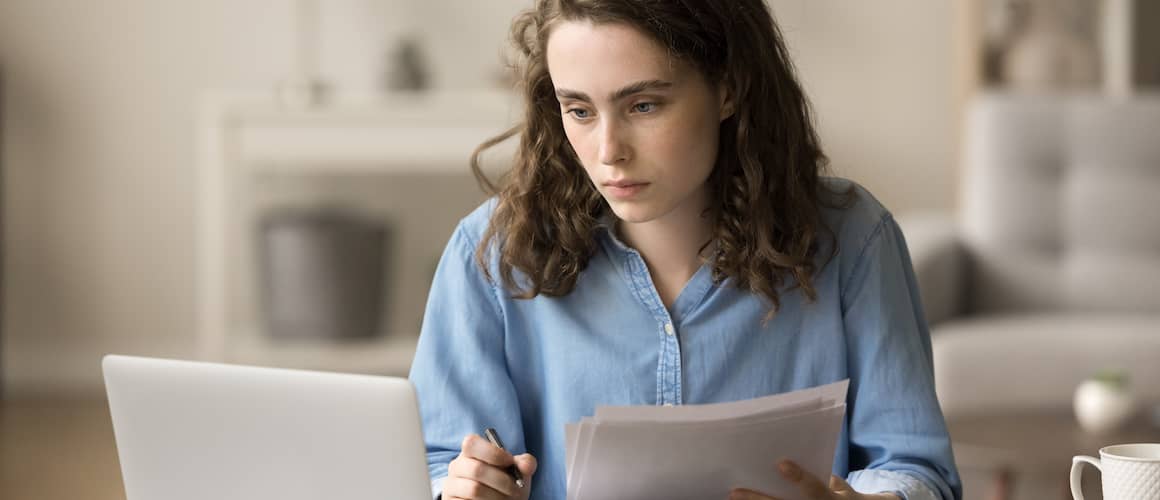 Woman stressed in front of laptop reviewing documents.