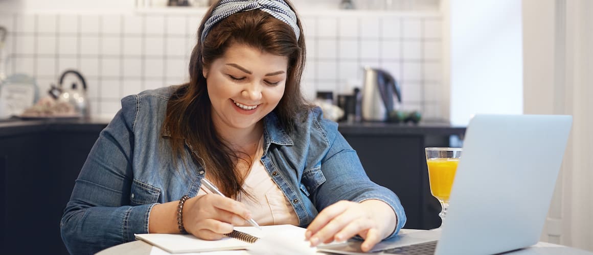 A woman working on a computer with papers scattered around.