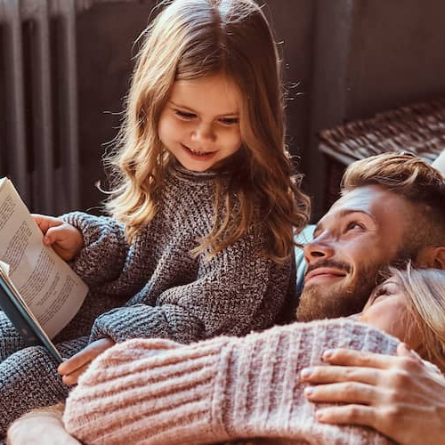 A couple enjoying with their daughter who is holding a book.