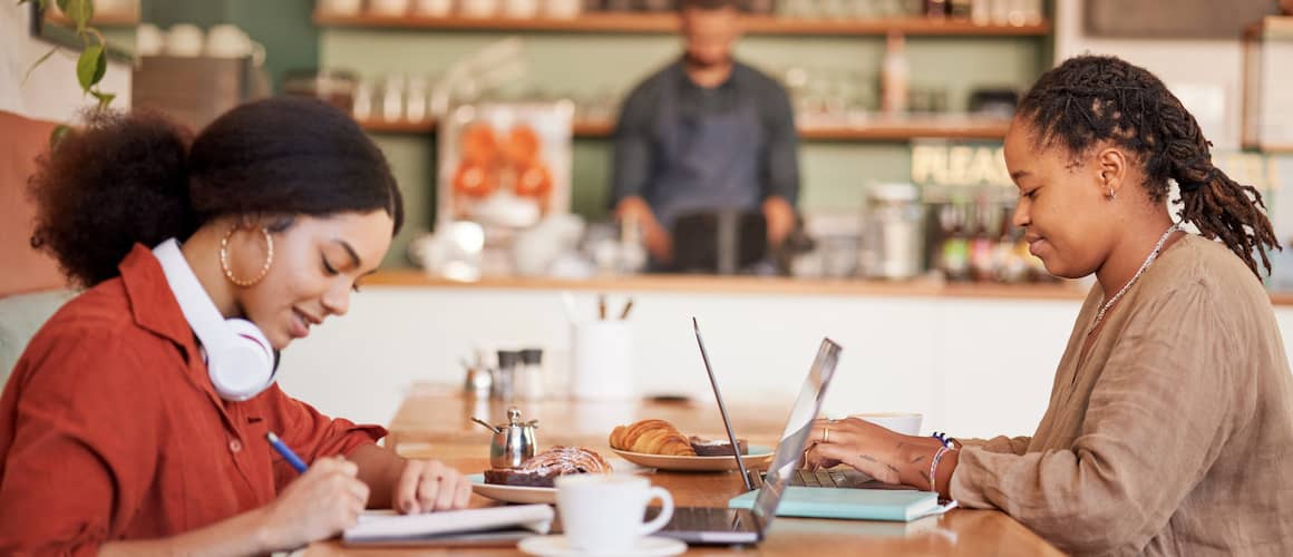 Two students at a cafe while working on their laptops.