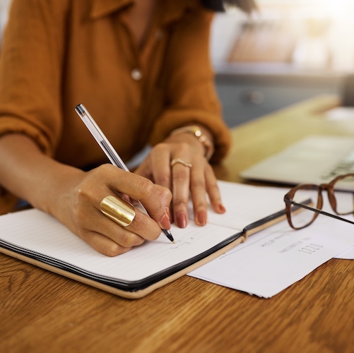 Woman calculating finances on paper with a laptop nearby.